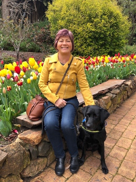 Colleen sitting on a small rock wall with her dog Rhian in front of tulips 