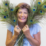 Colleen Ashby smiling through a bunch of peacock feathers