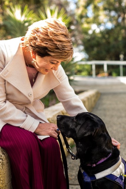 Picture of Colleen happily looking down on seeing eye labrador Rhian woth her hand on his shoulder