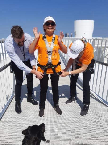 Picture of Colleen being strapped in to start her vertigo challenge  with a big smile and her hands up.